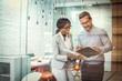 © Bojan - Through glass view of two smiling multi-ethnic business colleagues reviewing paper documents while standing in modern office