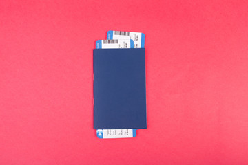 Blue passport with two flight tickets in it on pink background top view