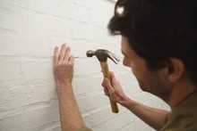 Male Carpenter Hammering Nail On Wall