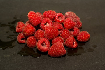 Lot of delicious raspberries on black stone