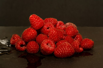 Lot of delicious raspberries on black stone