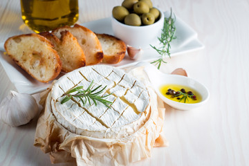 Wall Mural - Baked camembert cheese. Fresh Brie cheese and a slice on a wooden board with nuts, honey, rosemary, baguette bread grilled toasts and leaves. Brie type of cheese. Italian, French cheese.