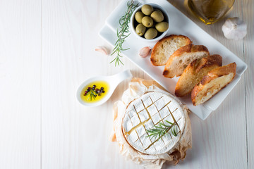 Wall Mural - Baked camembert cheese. Fresh Brie cheese and a slice on a wooden board with nuts, honey, rosemary, baguette bread grilled toasts and leaves. Brie type of cheese. Italian, French cheese.