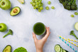 © lavrenkova - Frame flatlay with various green fruits and vegetables: lettuce, cucumber, avocado, broccoli, grapes, apples etc and woman's hand holding green juice on cement background. Healthy lifestyle concept