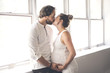 © Louis-Photo - Handsome man and his beautiful pregnant wife standing near the window at home