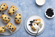 Individual blueberry loaf cakes with a serve on a plate and a bowl of blueberries and a bowl of cream.