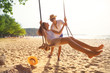 © tool51 - Romantic couple in love playing together on rope swing at summer beach for fun and happy smile. young man and woman on holidays or honeymoon