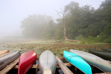 Wall Mural - morning autumn nature misty scene. scenic view with colorful kayaks on a lake on a foreground and tr