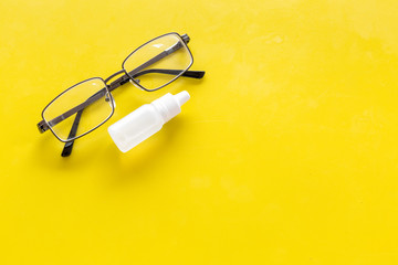 Canvas Print - Eye drops in small bottle near glasses on yellow background top view copy space