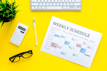 Weekly schedule of manager, office worker, pr specialist or marketing expert. Table with multicolored blocks on yellow office desk with computer, glasses, calculator top view