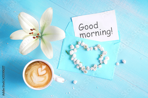 Cuadros en Lienzo Cup of cappuccino coffee, lily flower, heart and inscription Good morning on blue wooden background