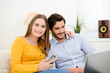 © W PRODUCTION - cheerful young couple on sofa at home websurfing and shopping online with laptop computer internet technology