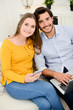 © W PRODUCTION - cheerful young couple on sofa at home websurfing and shopping online with laptop computer internet technology