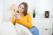 © W PRODUCTION - cheerful young woman relaxed on sofa making phone call at home with smartphone telephone technology