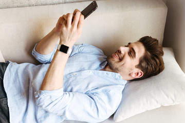 Wall Mural - Smiling young man using mobile phone while laying