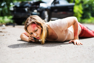 Wall Mural - Young injured woman lying on the road after a car accident, making a phone call.