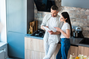 married couple using digital tablet together in kitchen, smart home concept