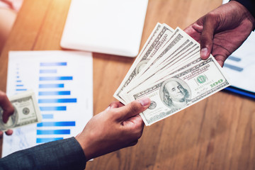 Close-up of businessman hand giving money to other hand.