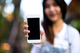 Fototapeta  - Mockup image of a woman holding and displaying a white mobile phone with a black screen with a blank screen on a table in a modern cafe. Ideas for working with communication tools.