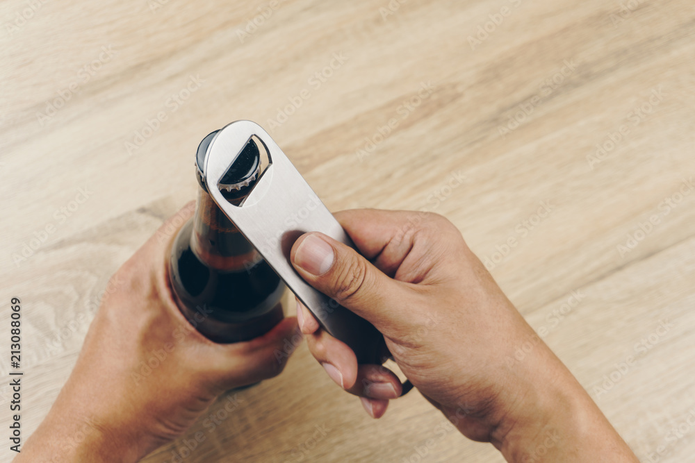 close up hand using a stainless steel bottle opener or bar blade to open a bottle of beer - obrazy, fototapety, plakaty 