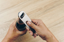 Close Up Hand Using A Stainless Steel Bottle Opener Or Bar Blade To Open A Bottle Of Beer