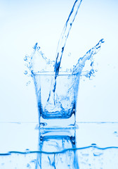 Splash from pouring water into the glass on a light blue background