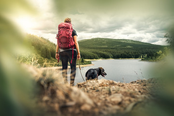 young woman with backpack and german shepherd dog puppy standing on mountain in front of forest and 
