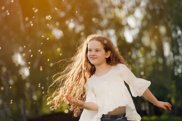 Wall Mural - curly little girl dancing in flying dandelions outdoors