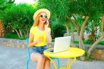 smiling woman talks on a smartphone, laptop computer on a cafe table