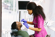 © sofiko14 - Dental and healthcare concept. Professional african american female dentist in pink medical suit examining teeth of young male patient