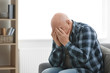 © New Africa - Depressed senior man sitting on sofa indoors