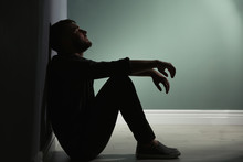 Depressed Young Man Sitting On Floor In Darkness