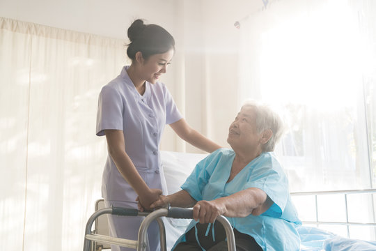 asian young nurse supporting elderly patient disabled woman in using walker in hospital. elderly pat