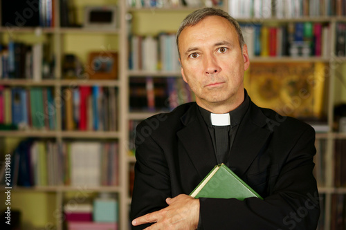 Fotografie, Obraz A good looking catholic priest is studying into his library