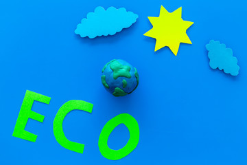 Wall Mural - Eco icon cutout near plastiline symbol of planet Earth, sun, clouds on blue background top view copy space