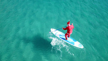 Aerial Drone Of Santa Claus Paddle Surfing In Australian Emerald Clear Sea Waters
