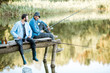 © rh2010 - Two male friends dressed in blue shirts fishing together with net and rod sitting on the wooden pier during the morning light on the lake