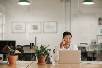 Asian businessman sitting in an office talking on his cellphone