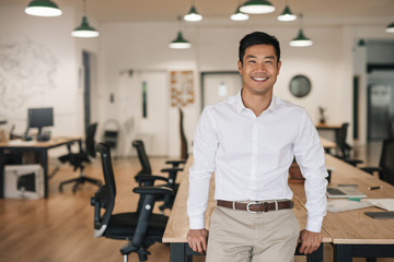 smiling asian businessman leaning on a table in an office