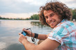 © iuricazac - Rear view of happy handsome male with curly hair taking photos of nature on his digital camera. Young smiling man wears casual shirt, with digital camera posing in the park. People, travel, lifestyle