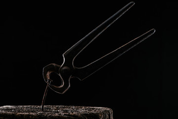  close up view of vintage pliers and nail in wooden stump isolated on black