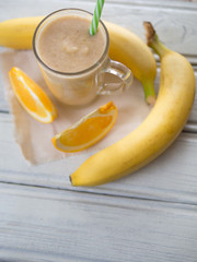 Wall Mural - fresh summer milkshake or orange and banana smoothie on wooden white table. top view
