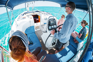 Young captain steers sailing boat in a tropical sea with three young ladies on board