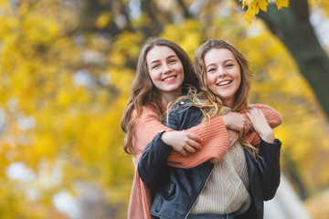 Young pretty girls having fun outdoors in autumn background. Cheerful friends in the fall time