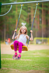 Wall Mural - Little blonde girl smiling swinging outdoors on a playgroung