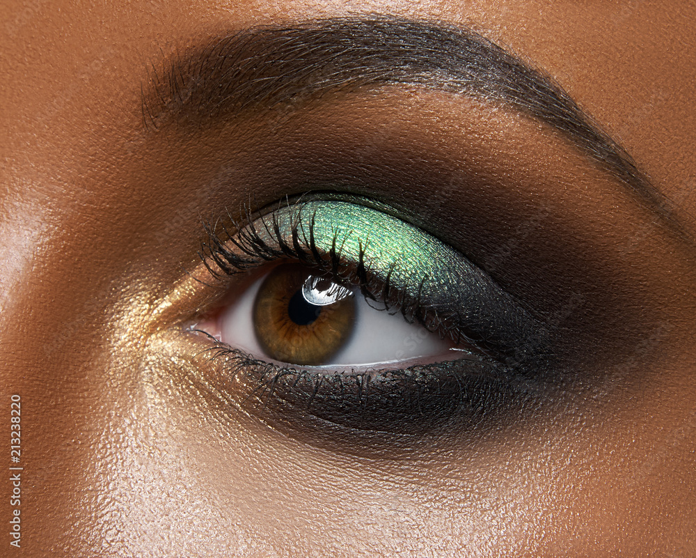 Macro and close-up creative make-up theme: beautiful female eye with green and golden shadows, black skin - obrazy, fototapety, plakaty 