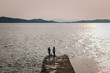 © WellStock - Man and woman standing on the stony pier and fishing. Beautiful sea view with mountains on sunset.