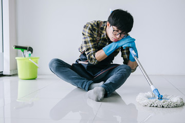 Wall Mural - Husband housekeeping and cleaning concept, tired man in blue rubber gloves wiping dust using mop while cleaning on floor at home