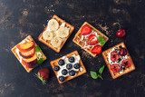 Fototapeta  - Belgian waffles with blueberries,strawberries,peaches, cherries and banana. Homemade waffles on a dark rustic background. The view from the top,flat lay.