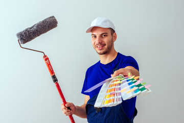 Painter man at work with a paint roller and color samples. Home renovation and decoration concept.